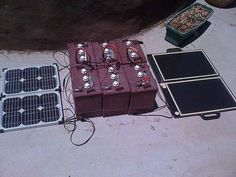 solar panels and batteries on the ground next to an open box with some wires in it