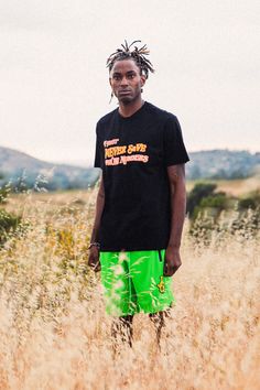 a man standing in the middle of a field wearing green shorts and a black t - shirt