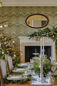 a dining room table set for christmas dinner with candles and greenery on the table