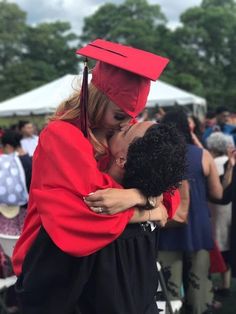 a woman in a red graduation gown hugging another woman wearing a black cap and gown