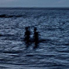 three people standing in the ocean at night