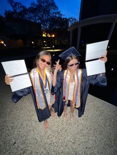 two girls in graduation gowns holding up their diplomas