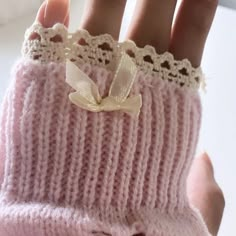 a woman's hand wearing a pink knitted mitt with a white bow