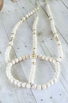 two white beaded necklaces sitting on top of a wooden table next to a vase