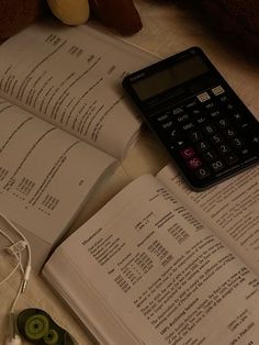 an open book with a calculator and headphones on it next to some books