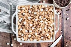 a pan filled with marshmallows on top of a wooden table next to a bowl of chocolate chips