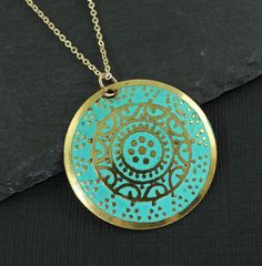 Turquoise and gold medallion necklace features a round gold disc embossed with an ornate design and colored with turquoise enamel. Pendant has a distressed feel with some dark areas on the pendant. This is part of its style. Pendant is 1 3/16 inches in diameter (30mm). Your choice of chain lengths - 16 or 18 inches. Chain is gold plated. Find more necklace styles here - https://www.etsy.com/shop/CharleneSevier?ref=hdr_shop_menu&section_id=10084290 Sign up for my newsletter! Copy and paste this link in your browser - http://eepurl.com/iSq7Wc ---------------------------------- PLEASE READ: This item is not intended for children where choking is a hazard. ---------------------------------- Green Coin Pendant Medallion Jewelry, Bohemian Gold Necklace With Patina, Blue Coin Pendant Jewelry, Gold Circle Jewelry For Festivals, Gold Circular Jewelry For Festivals, Gold Circular Festival Jewelry, Blue Medallion Necklace With Coin Pendant, Turquoise Engraved Round Pendant Necklace, Bohemian Engraved Turquoise Necklaces