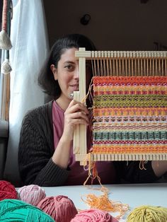 a woman sitting in front of a weaving machine with several balls of yarn behind her