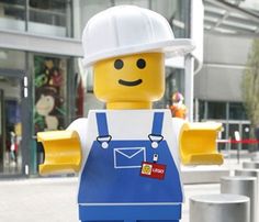 a lego man with a white hat and blue overalls standing in front of a building