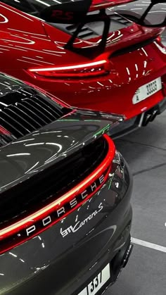 two red porsches are parked next to each other in a showroom, one has its trunk open