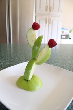 a white plate topped with green apples and raspberries in the shape of a tree