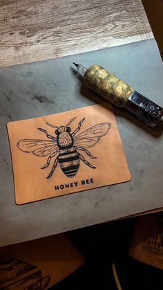 a honeybee sticker sitting on top of a wooden table next to a pen