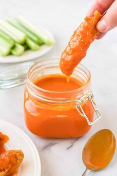 a person dipping sauce into a jar filled with chicken wings on top of a white plate