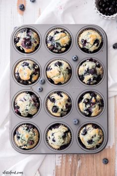 blueberry muffins in a muffin tin on a wooden table with fresh blueberries