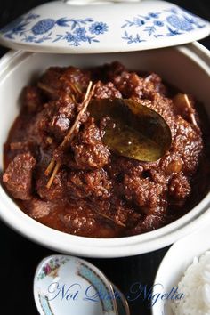 a bowl filled with beef and rice on top of a table next to spoons