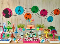 a table topped with lots of cakes and desserts covered in paper music note decorations