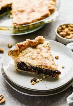 a slice of pie sitting on top of a white plate next to a bowl of nuts