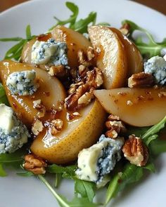 a white plate topped with sliced pears and blue cheese on top of lettuce