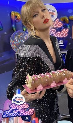 a man and woman holding a cake with frosting on it in front of balloons