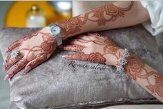 two hands holding each other with henna tattoos on their arms and wrist, sitting on a pillow