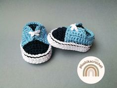 a pair of crocheted blue and white baby shoes on a gray surface with a rainbow sticker