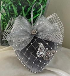 a black and silver heart shaped box with a butterfly on the front, sitting next to a green plant