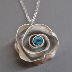 This pendant has a unique shape: a three-dimensional spiral reminiscent of a rose. The spiral showcases an apatite gemstone in a striking blue. The pendant can also be made with a blue topaz or other gemstones in various colors, please convo me if you'd like a different stone. I hand-forge the necklace starting from a flat sheet of sterling silver. The 6mm faceted gemstone in a brilliant cut is set in a sterling silver tube setting - the most secure of stone settings. I give the pendant my signa Tube Setting Pendant, Stone Setting Jewelry Design, Tab Setting Jewelry, Tube Setting Jewelry, Silver Pendant Necklace Unique, Metal Clay Designs, Stone Settings Jewelry, Contemporary Jewellery Necklace, Eine Rose