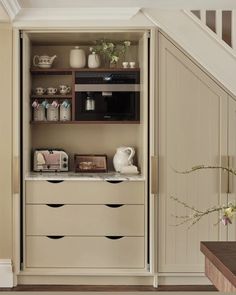 an open cabinet in the corner of a room next to a stair case with dishes and cups on it