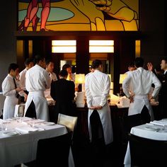 several chefs are standing in front of tables with white tablecloths and black chairs