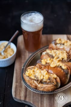 two hot dogs covered in macaroni and cheese on a plate next to a glass of beer