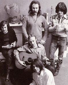 four people are posing for a photo while one man is holding an acoustic guitar in front of them