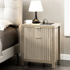 a nightstand with a lamp on it next to a bed