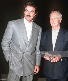 two men standing next to each other in suits and ties, one with a moustache on his face