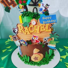 a birthday cake that is decorated with animals and letters on it's side, sitting on a green tablecloth