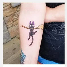 a person with a cat tattoo on their arm holding a broom and wearing a black shirt