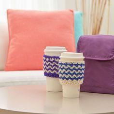 two coffee cups sitting on top of a table next to a purple and pink pillow