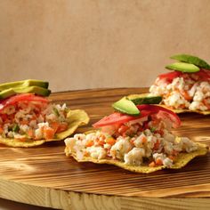 three tortilla shells topped with vegetables and avocado on a cutting board