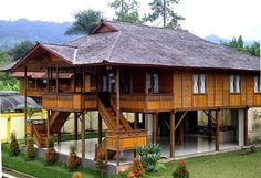 a large wooden house sitting in the middle of a lush green field next to mountains