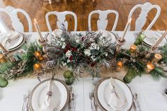 the table is set with white plates, silverware and greenery for christmas dinner