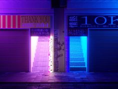 an empty street at night with closed shutters and neon lights on the side of buildings