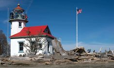 a white lighthouse with a red roof surrounded by driftwood and an american flag flying in the background