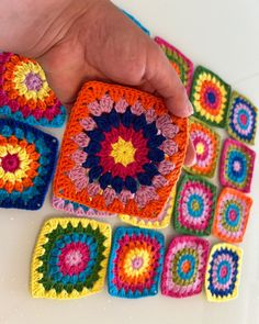 a hand is holding a crocheted square in front of several granny granny squares