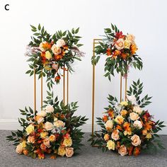 two tall floral arrangements on gold stands with leaves and flowers in orange, red, yellow and white colors