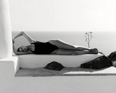 a woman laying on top of a white wall next to a plant in the air