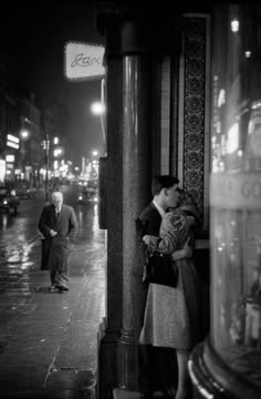 a man and woman are kissing on the street at night in front of a store