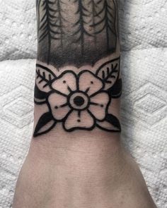 a hand with a black and white tattoo design on it's left wrist, which has trees in the background