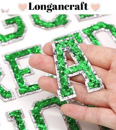 a hand holding a green and white letter shaped brooch with letters in the background