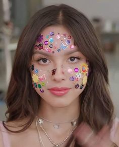 a woman with flowers painted on her face holding two fingers up in front of her face