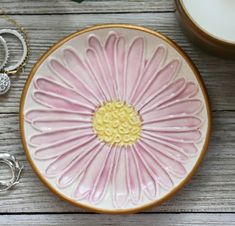 a pink and yellow flower on a white plate next to some silver rings, bracelets and a candle