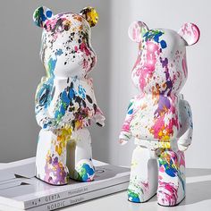 two colorful painted teddy bears sitting next to each other on top of a white table